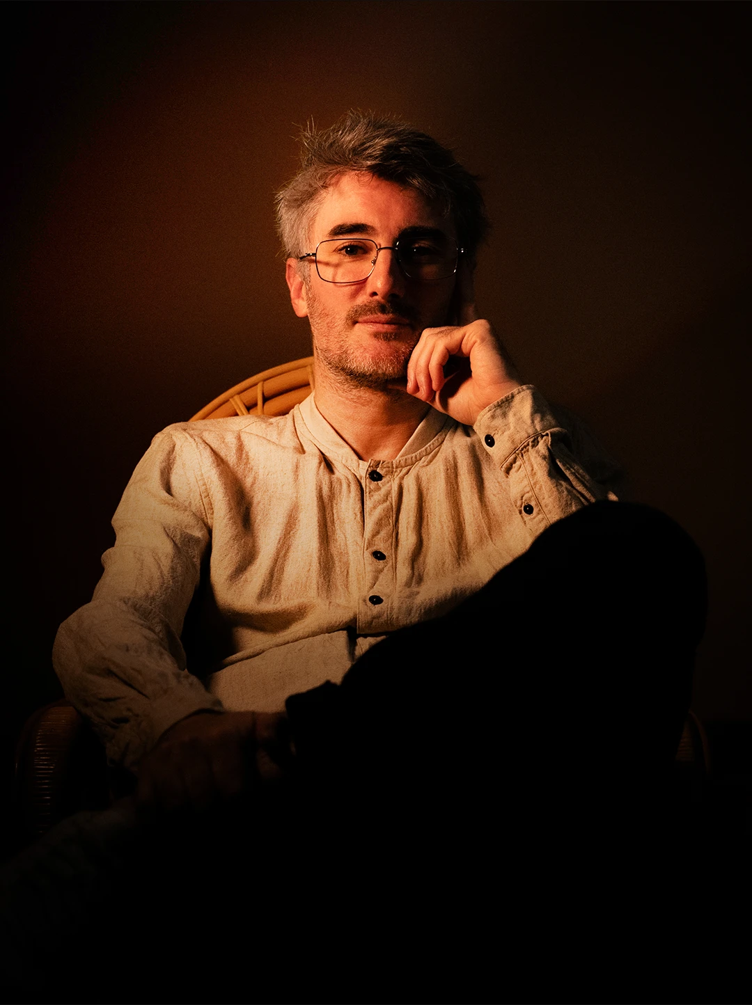 Jimmy – fondateur et directeur créatif de Heji, studio créatif à Rambouillet Portrait de Jimmy, fondateur du studio créatif Heji, assis en lumière chaude ambrée — page À propos Heji