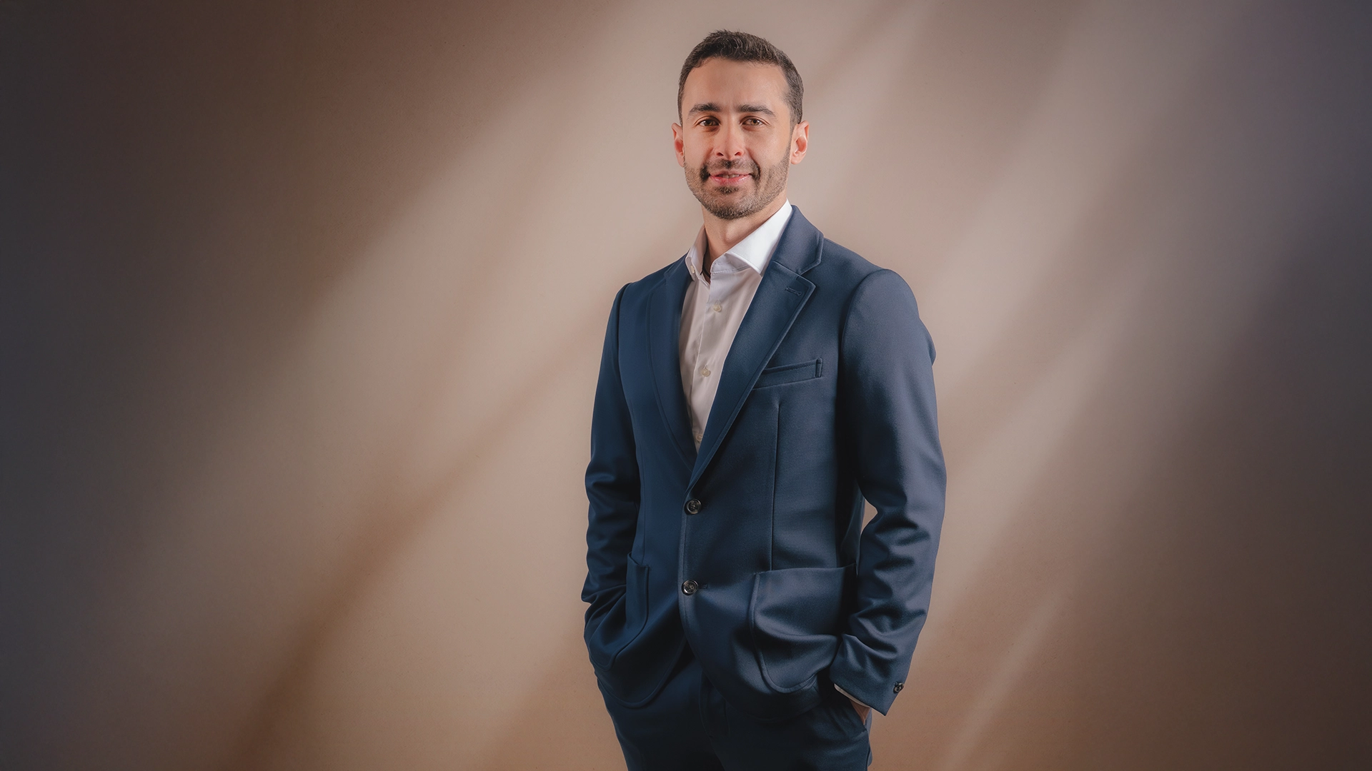 Photographie portrait corporate – homme en costume, studio lumière brossée Portrait corporate en studio d'un homme en costume bleu marine sur fond brossé beige et gris — photographie portrait corporate par Heji